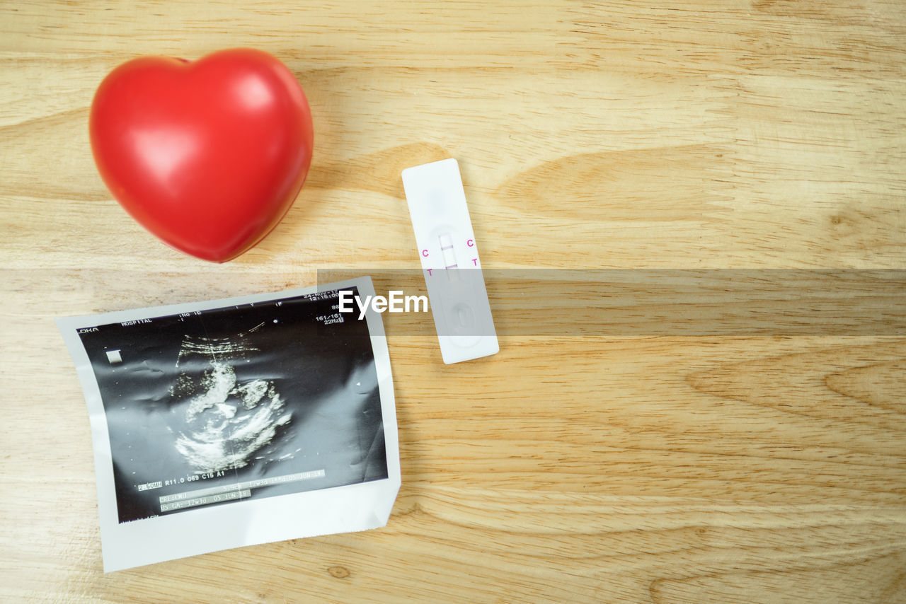 High angle view of ultrasound with heart shape and pregnancy test kit on wooden table