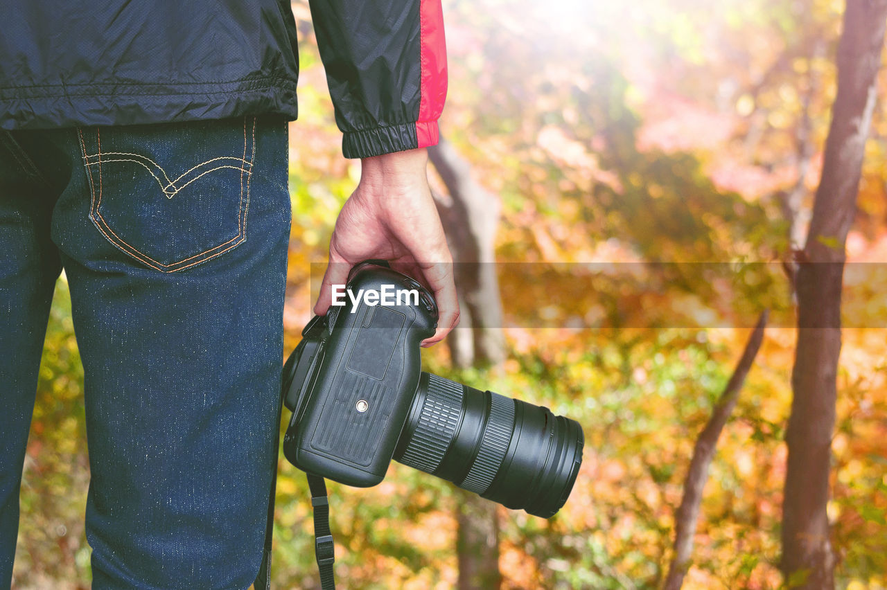 Midsection of man holding camera while standing in forest