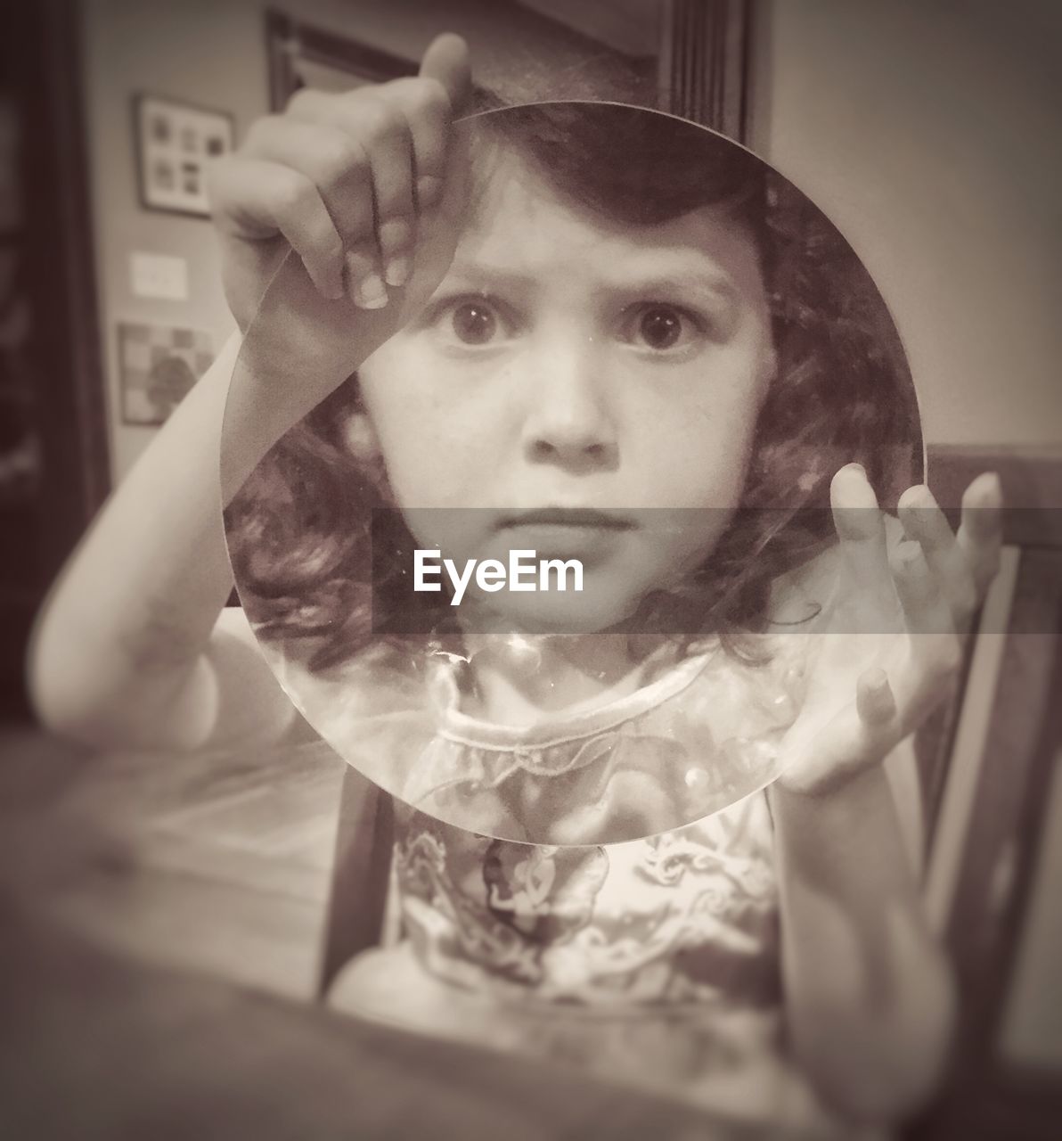 Girl holding magnifying glass while sitting on chair at home