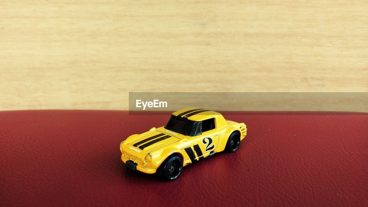 HIGH ANGLE VIEW OF TOY CAR ON TABLE AGAINST GRAY BACKGROUND