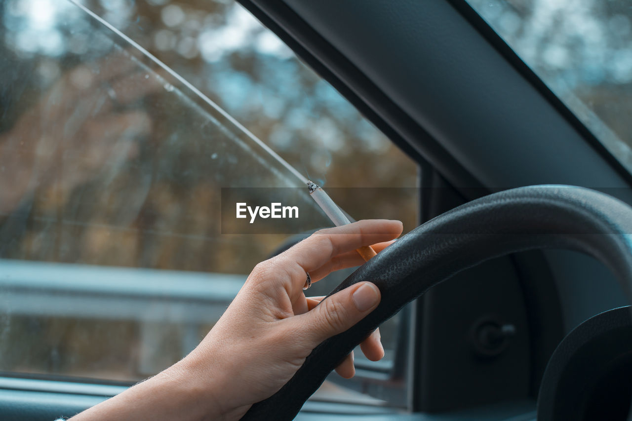 Cropped hand of person holding cigarette while driving car
