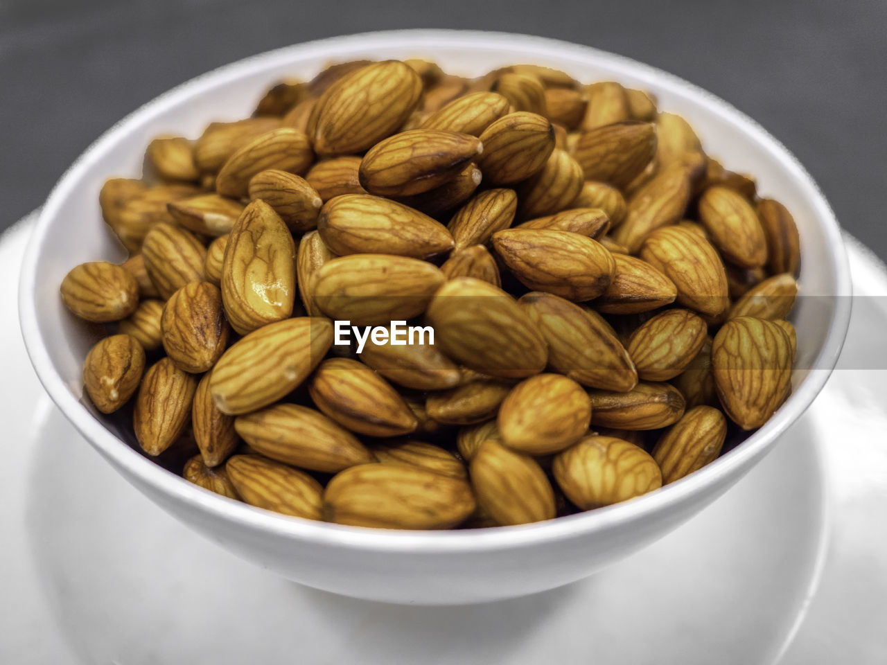 Closeup fresh almonds in white bowl on dark table background, 