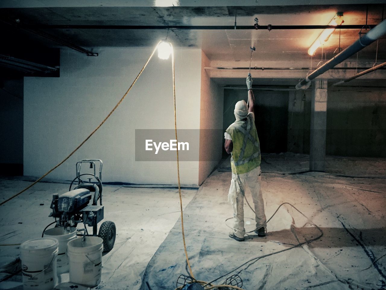 Rear View Of Man Spraying Paint On Ceiling On Eyeem