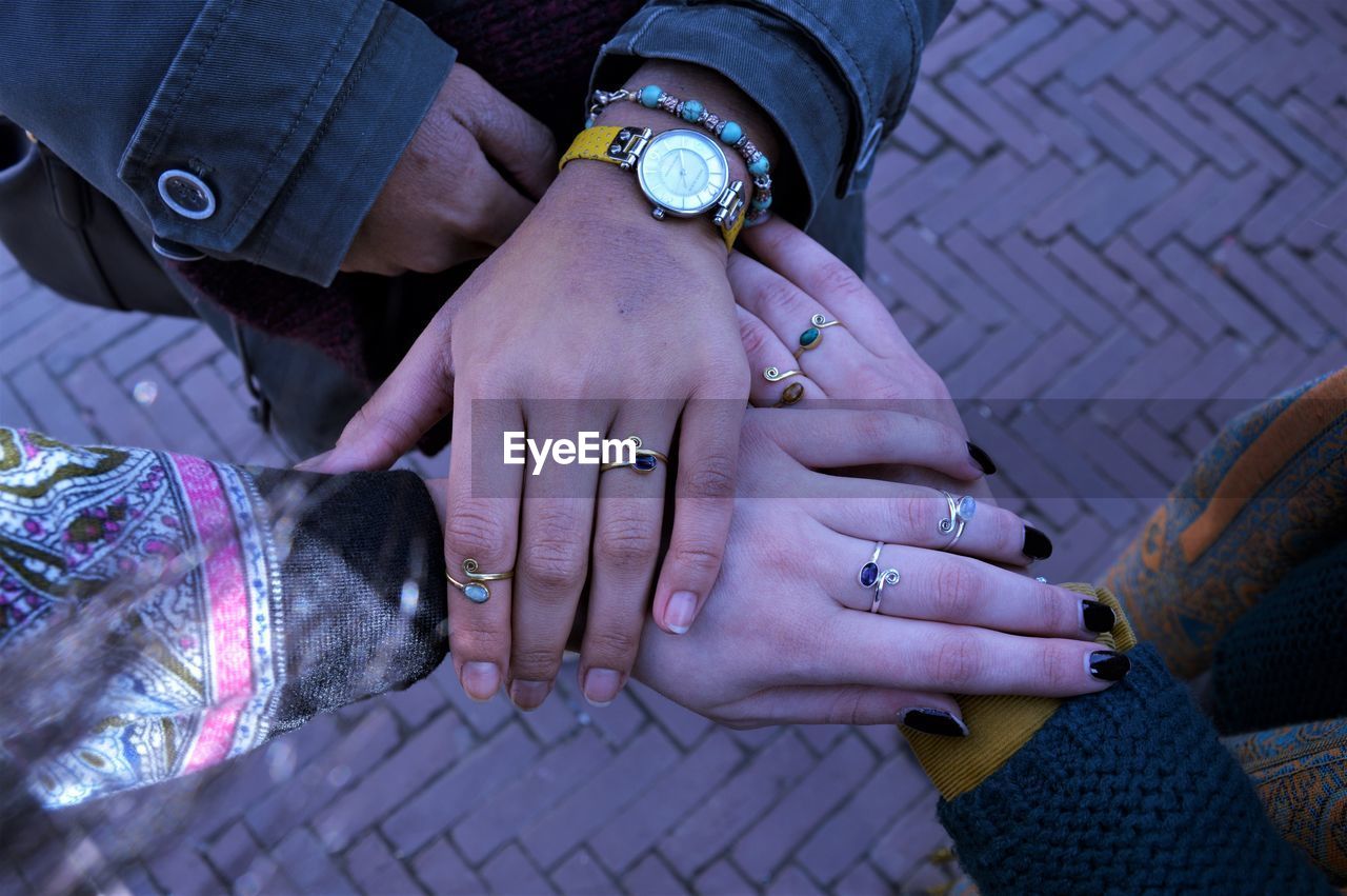 Directly above shot of friends wearing finger rings while stacking hands on street