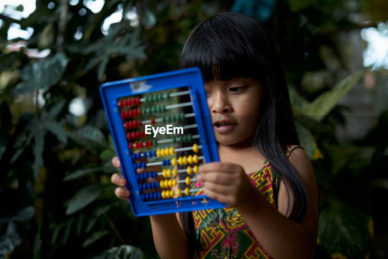 Close-up of girl playing with abacus against plants