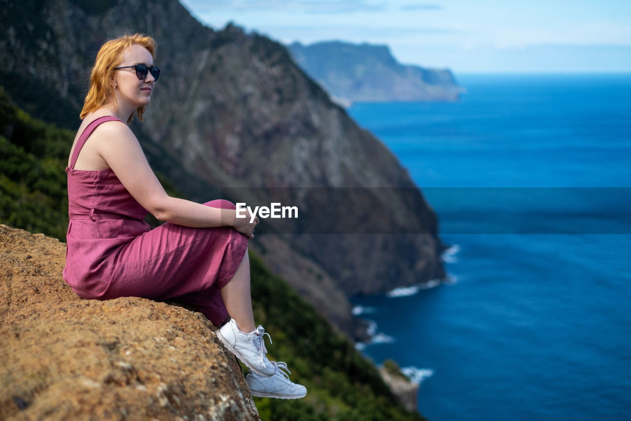 Woman looking away while sitting on cliff by sea