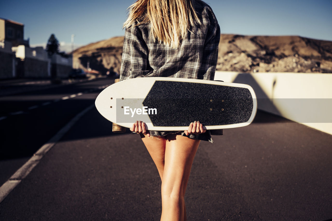 Midsection of woman with skateboard standing on road