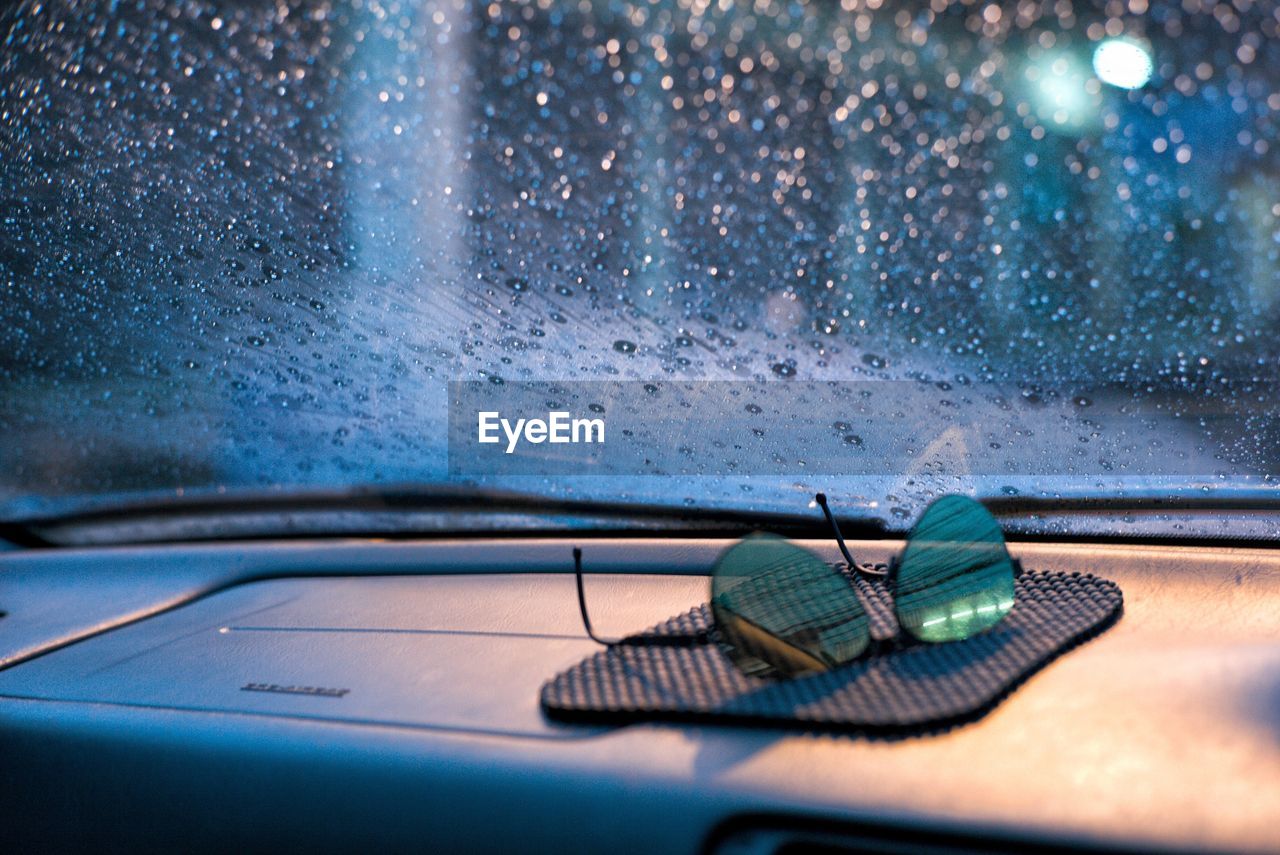 Raindrops and moisture on the car front glass with blurred sunglasses in foreground at rainy night