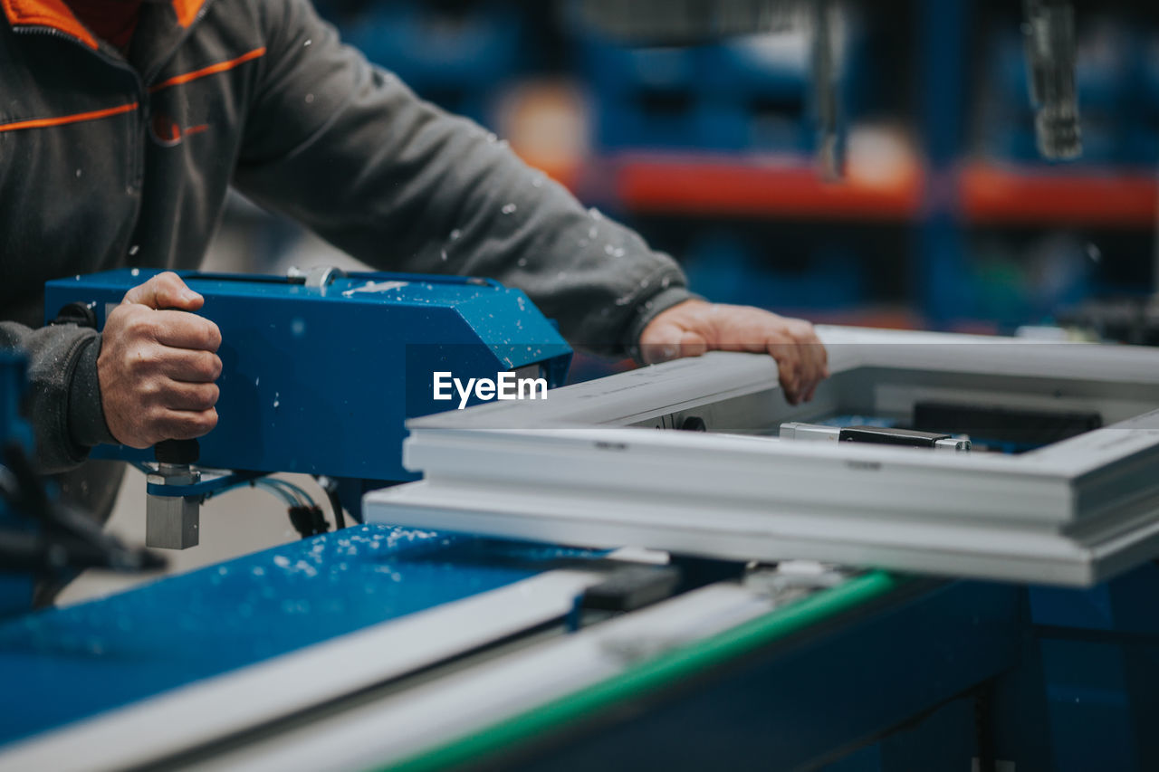 Midsection of mature man using equipment in factory