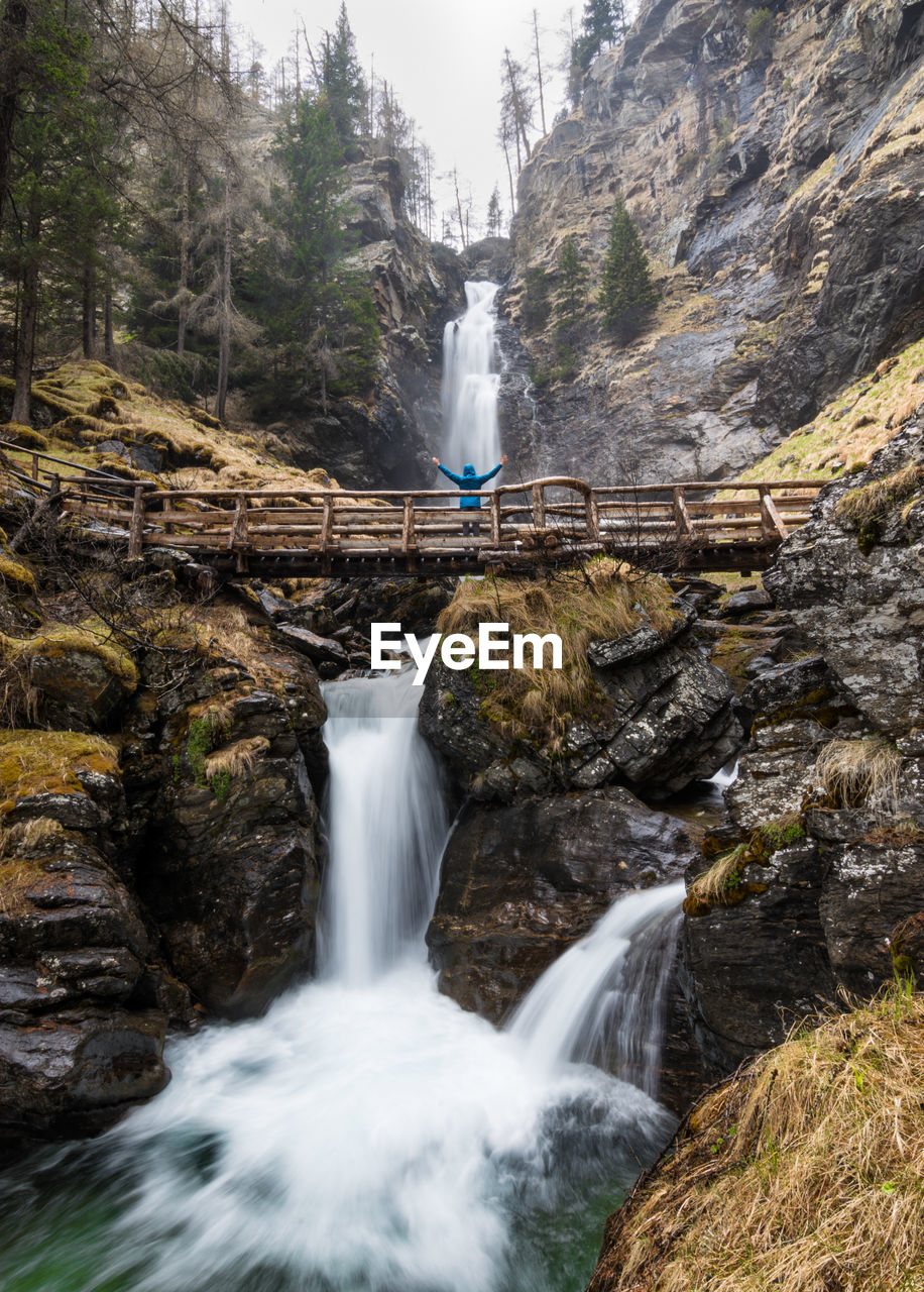 Low angle view of person standing on footbridge against waterfall