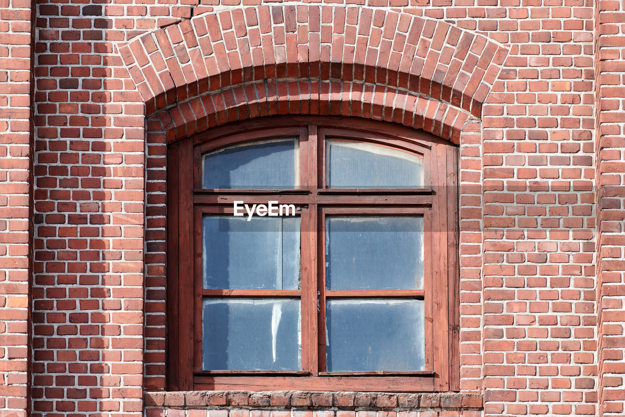 One arched glass window on old red brick wall. vintage window in brown wooden frame