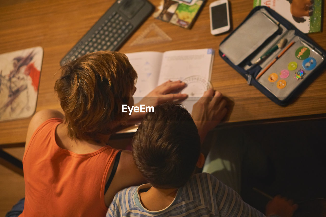 High angle view of mother assisting son in homework at table