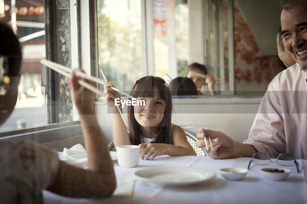 Happy granddaughters with grandfather sitting in restaurant