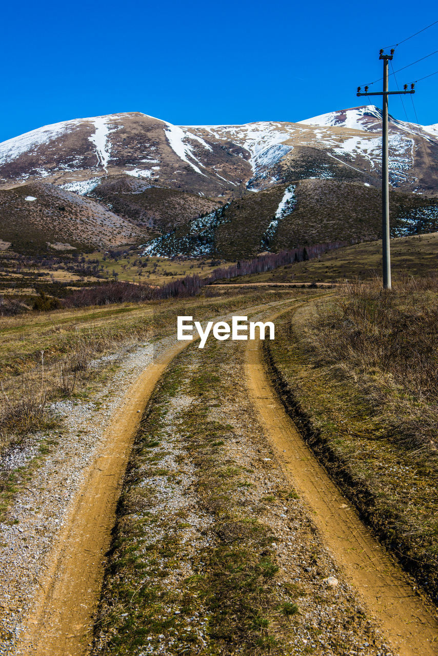 Road amidst snowcapped mountains against clear sky