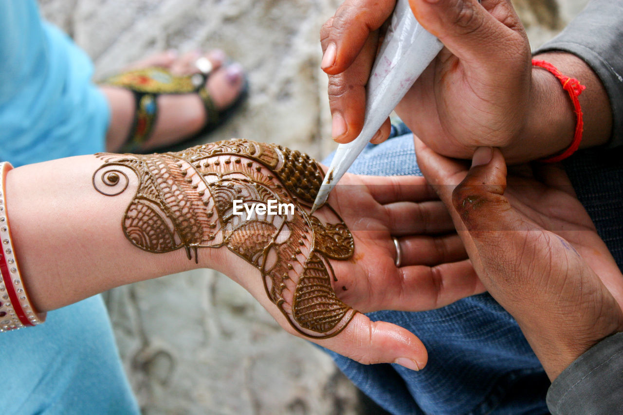 Cropped image of man making henna tattoo on woman hand