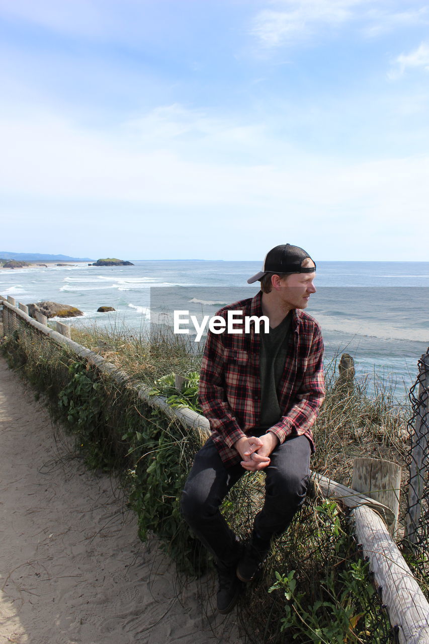 Man looking away while sitting on retaining wall