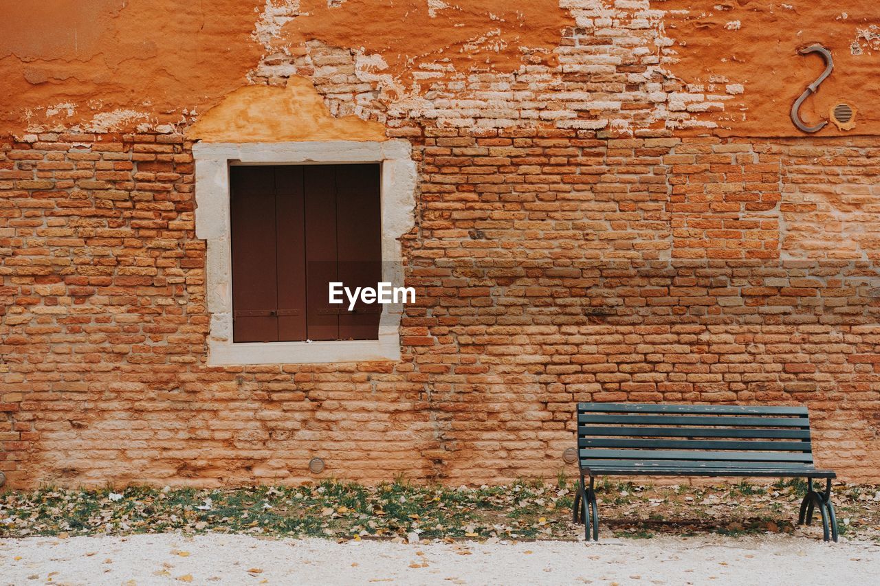 Empty bench against brick wall of old building