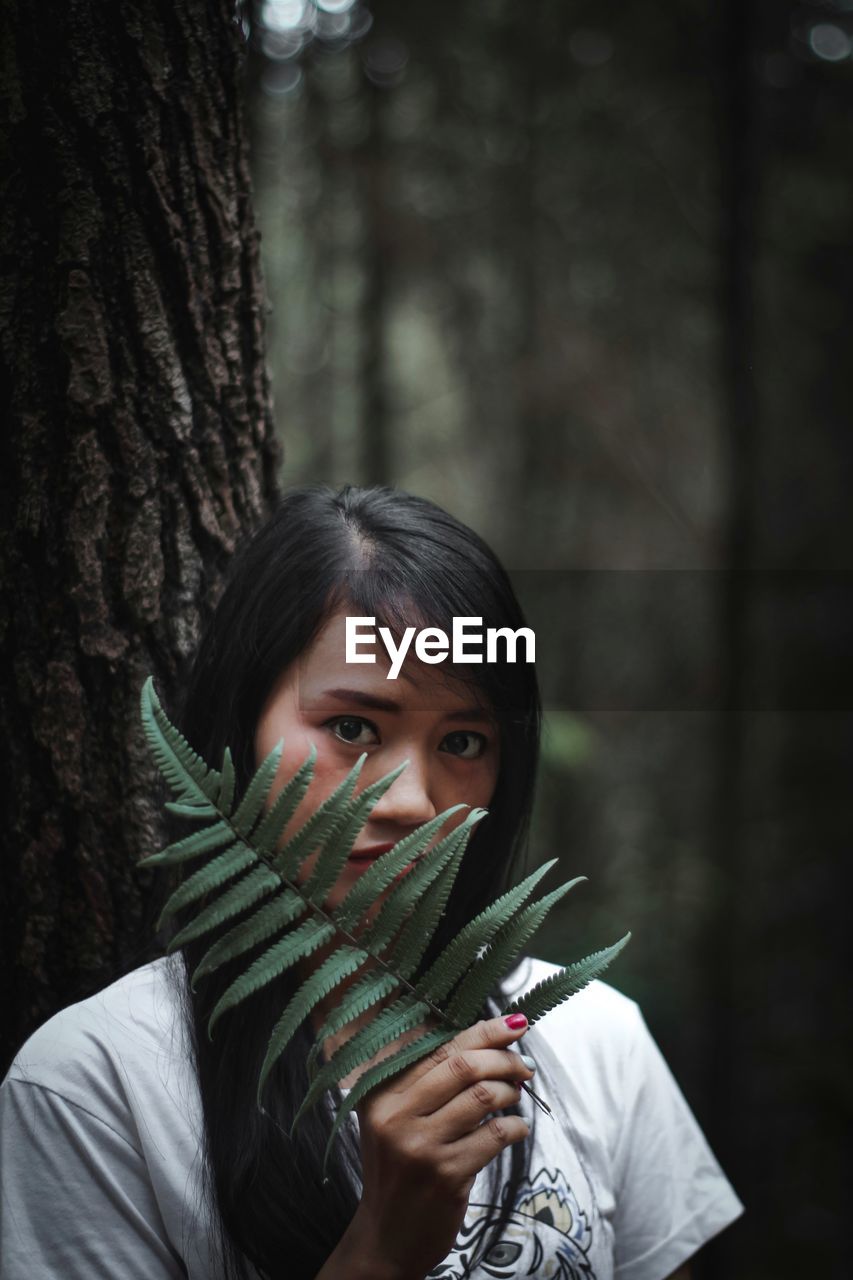 Portrait of happy girl holding tree trunk in forest