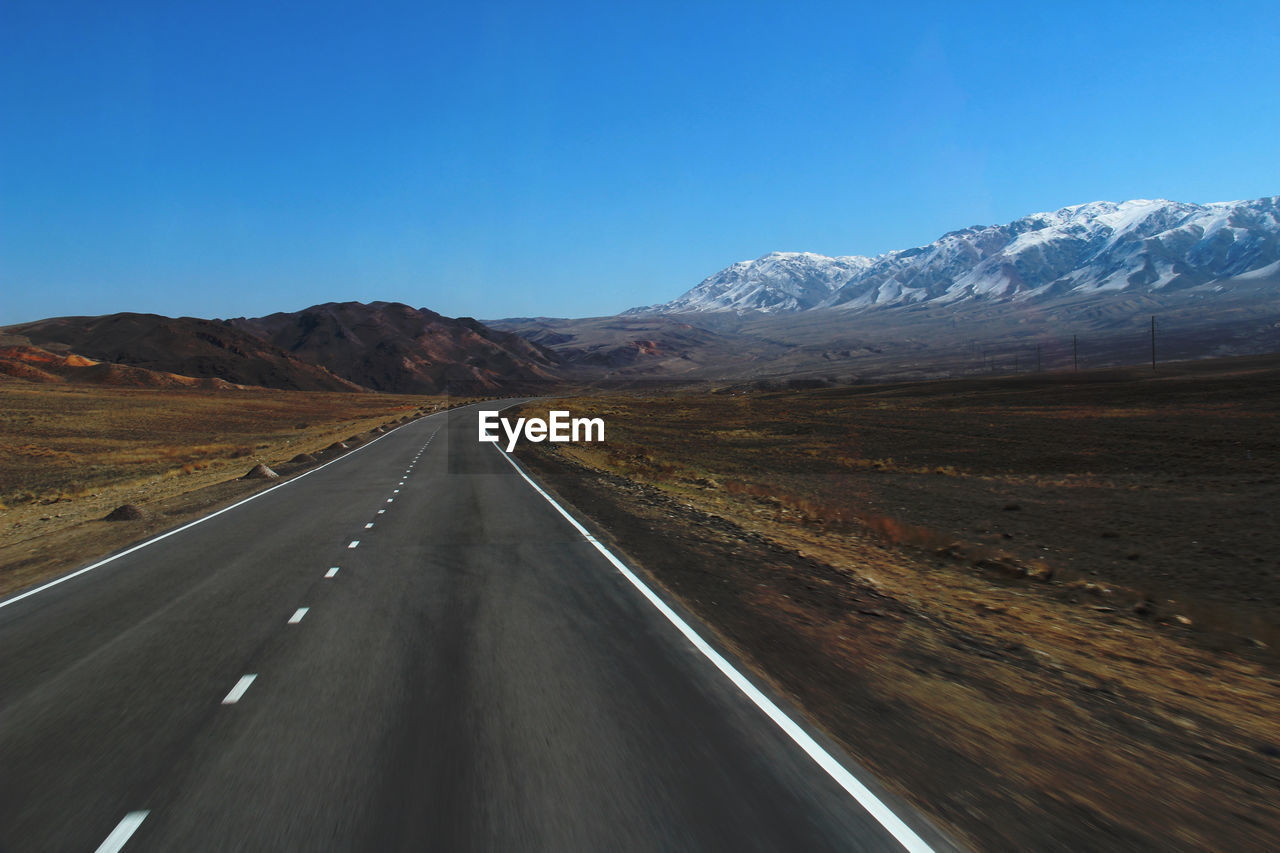 Highway with a turn in the mountains with a snow-covered mountain range, spring, sunny, day