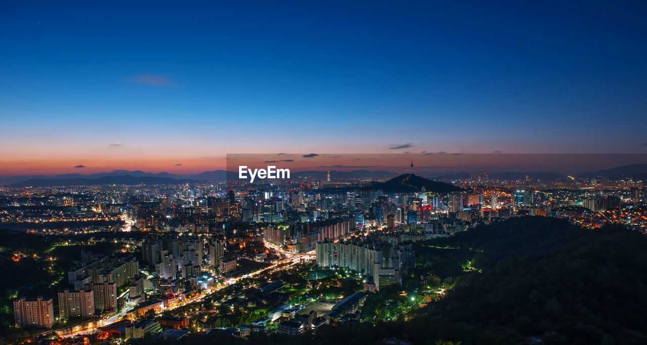 HIGH ANGLE VIEW OF ILLUMINATED CITY BUILDINGS AGAINST SKY