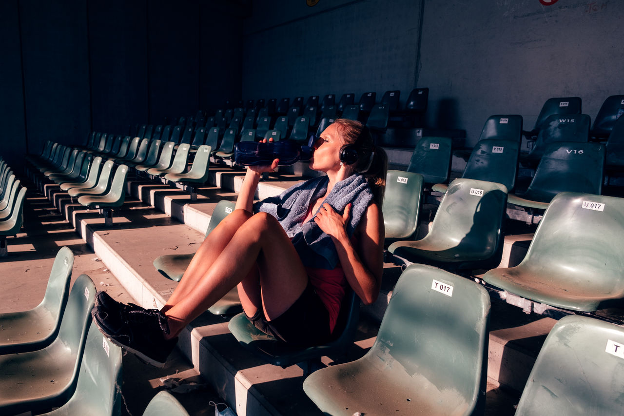 Athletic woman taking rest after workout - fit woman in sportswear sitting on stadium seats