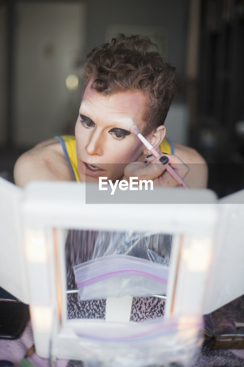 Man looking in mirror and applying drag cosmetics