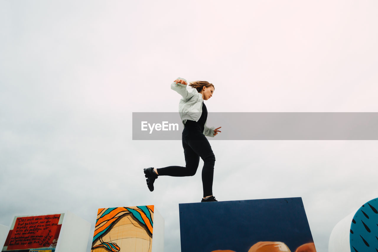 Low angle view of woman jumping over wall against sky