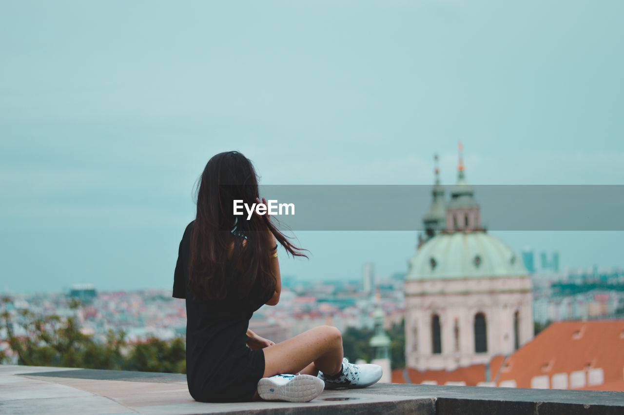 Woman sitting against sky in city