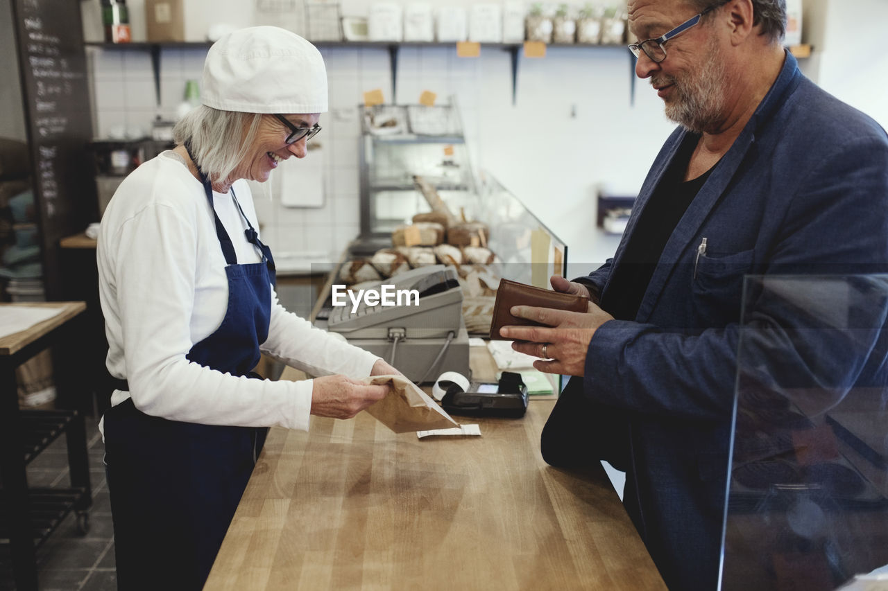 Male customer paying female baker while standing at checkout corner in bakery