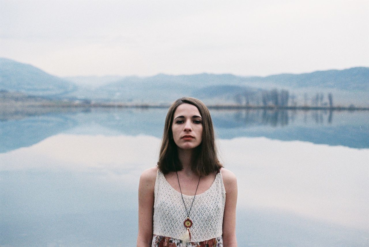 Portrait of woman standing by lake against sky