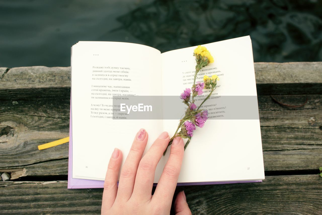 Cropped image of hand holding book against white wall