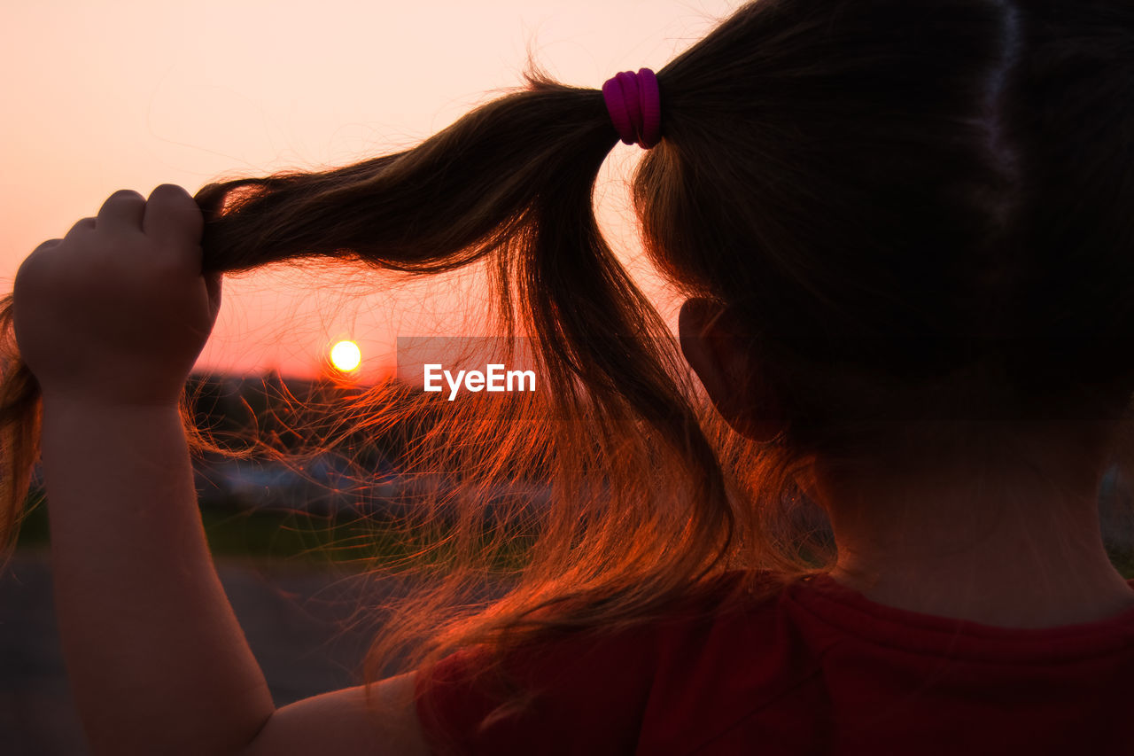 Rear view of girl holding pigtails during sunset