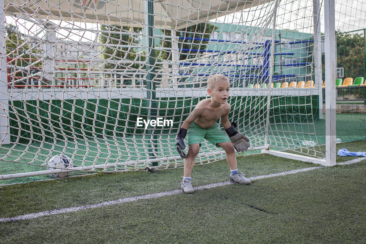 Full length of shirtless boy playing soccer on land