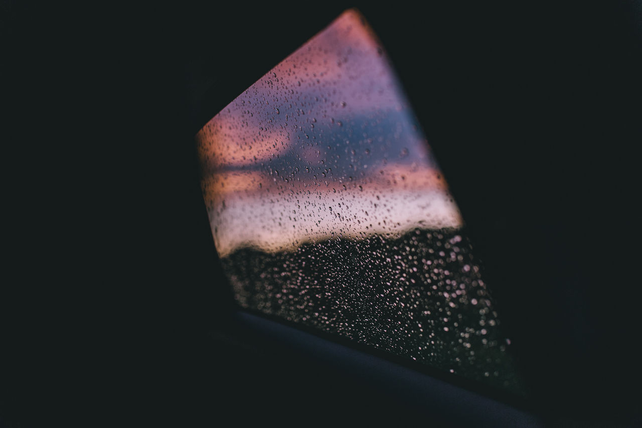 CLOSE-UP OF DROPS ON CAR WINDOW AGAINST BLACK BACKGROUND