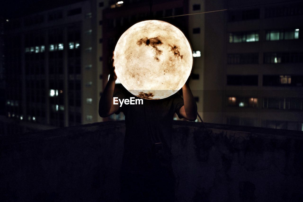 Man holding artificial moon at night