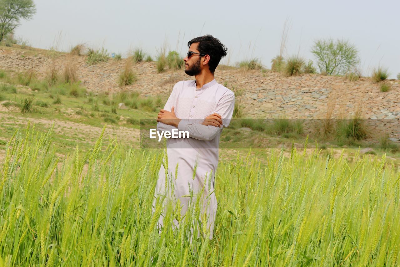 plant, one person, adult, agriculture, field, nature, grassland, land, landscape, grass, meadow, prairie, rural scene, growth, crop, men, environment, natural environment, occupation, rural area, paddy field, young adult, standing, three quarter length, sky, casual clothing, looking, tranquility, day, beauty in nature, outdoors, green, cereal plant, contemplation, scenics - nature, lifestyles, clothing, tranquil scene, leisure activity, non-urban scene, holding