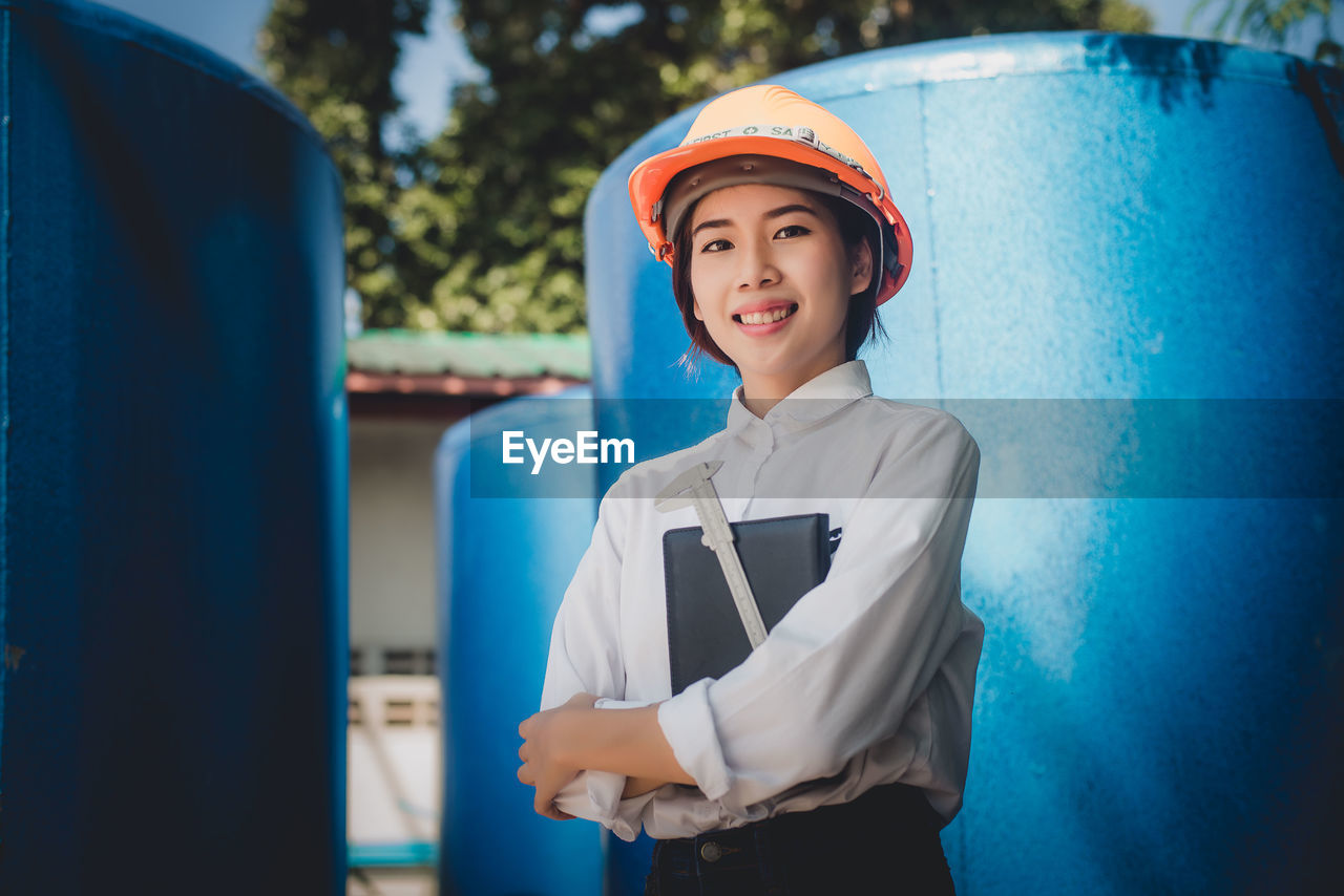Portrait of smiling engineer standing by storage tanks at factory