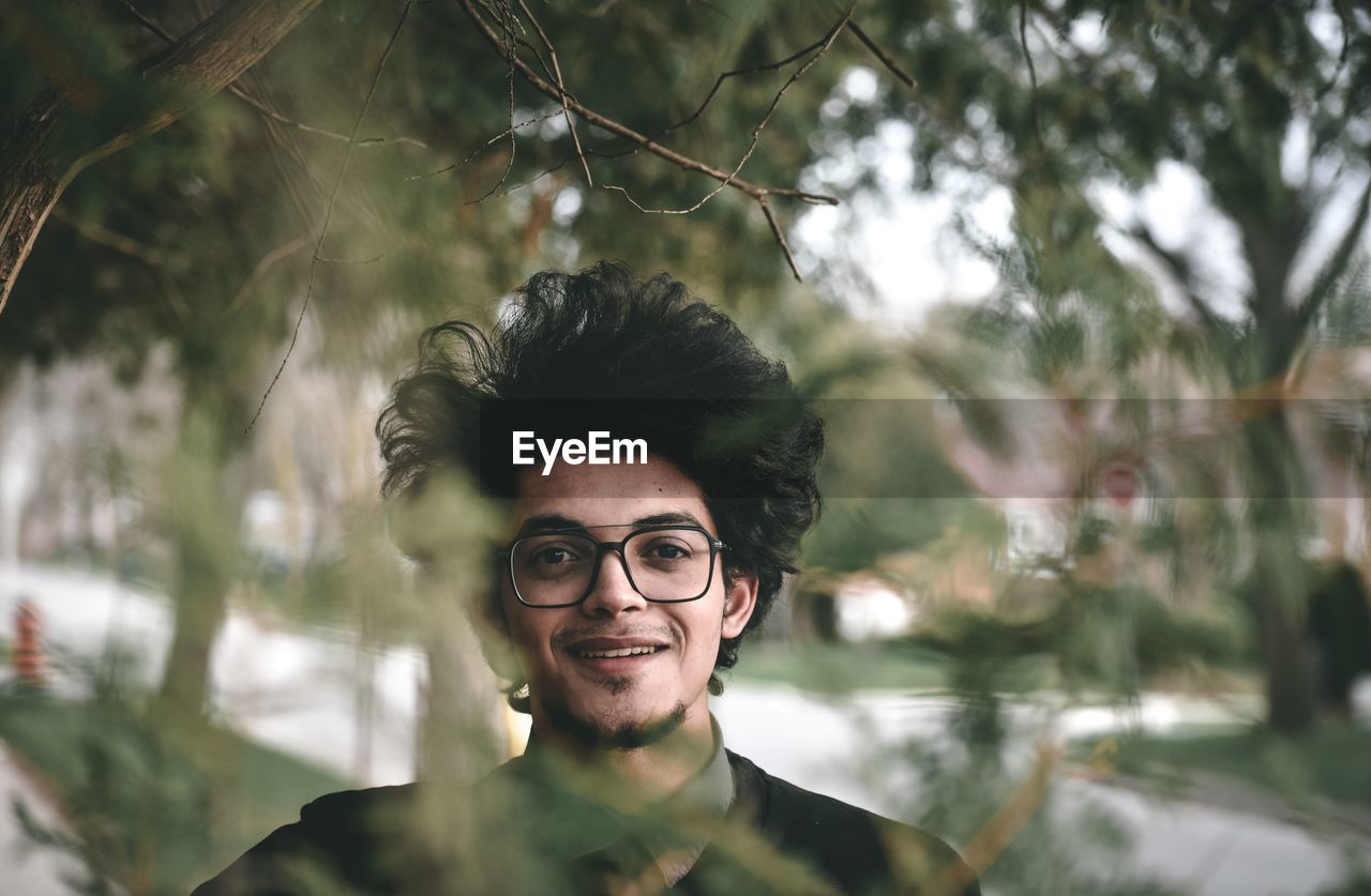 PORTRAIT OF YOUNG MAN WEARING EYEGLASSES AND TREES