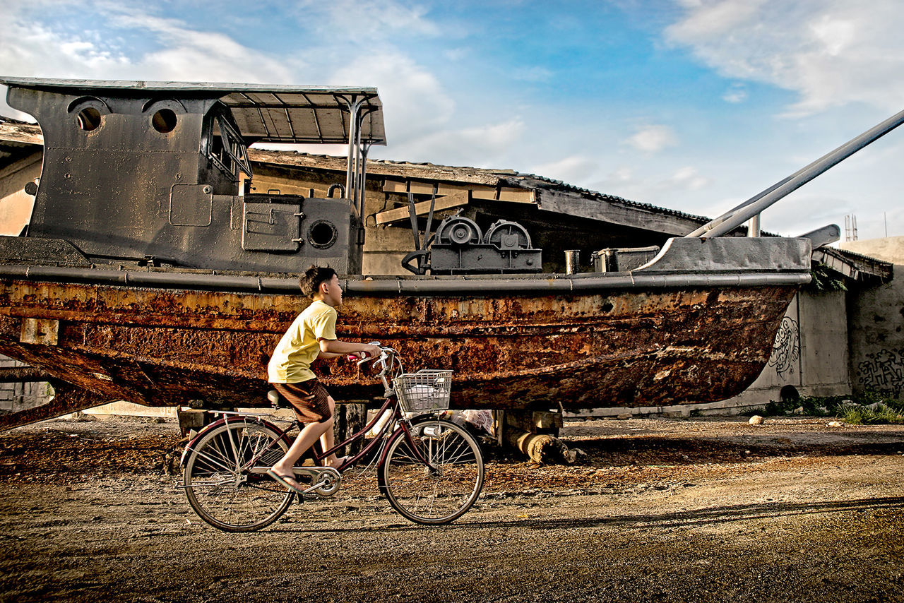 Side view of boy cycling by abandoned boat on street