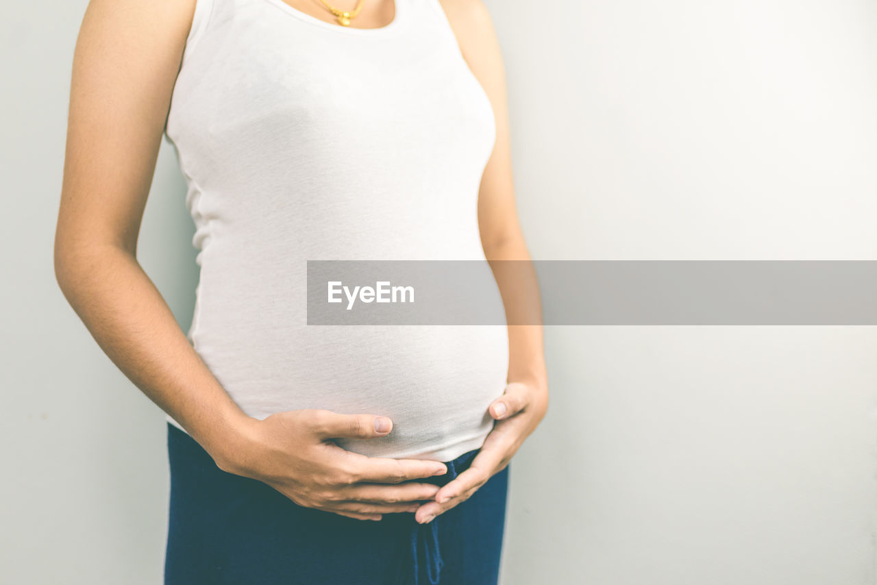 Midsection of pregnant woman touching stomach against gray background