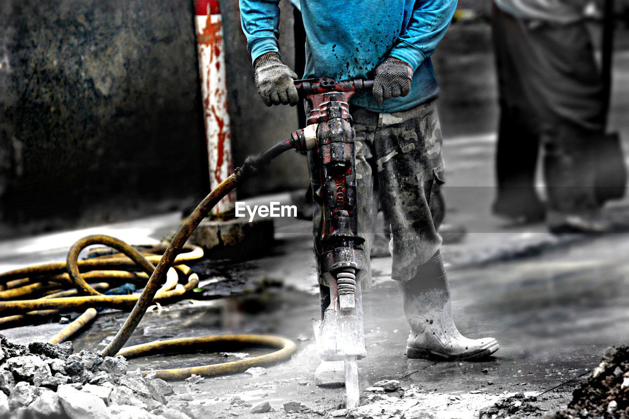 Low section of messy worker with jackhammer on street