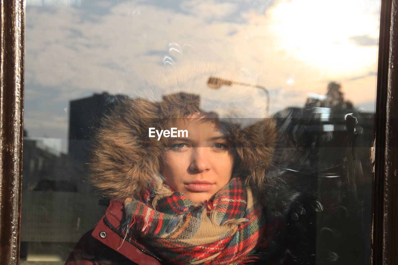 Portrait of young woman wearing warm clothing seen through window