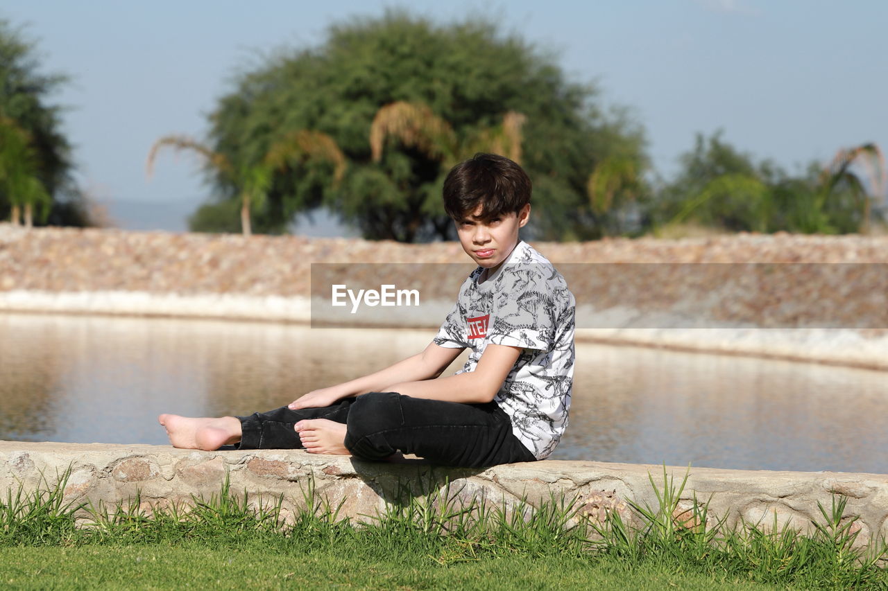 Boy sitting on lake against plants