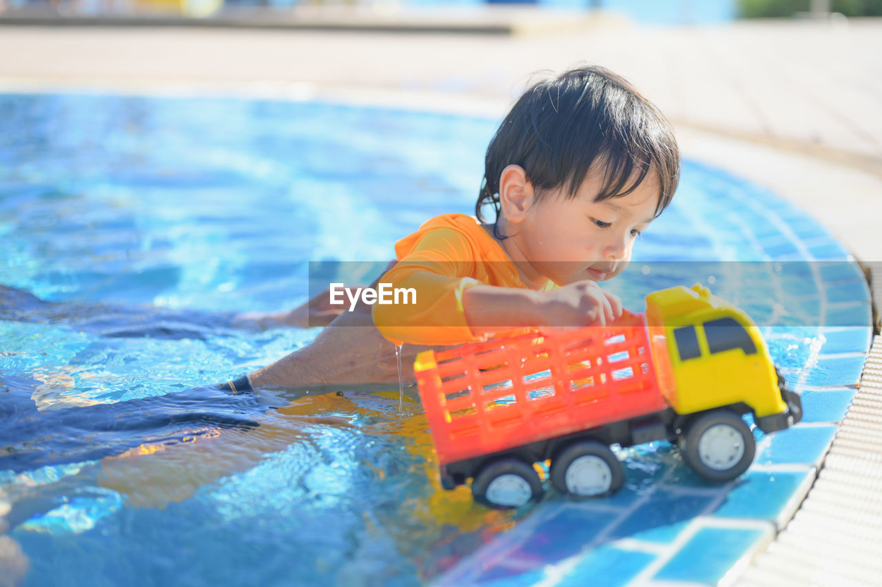 portrait of boy playing with toy car in swimming pool