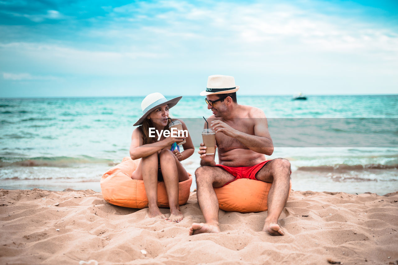 Mature couple having drinks while sitting at beach