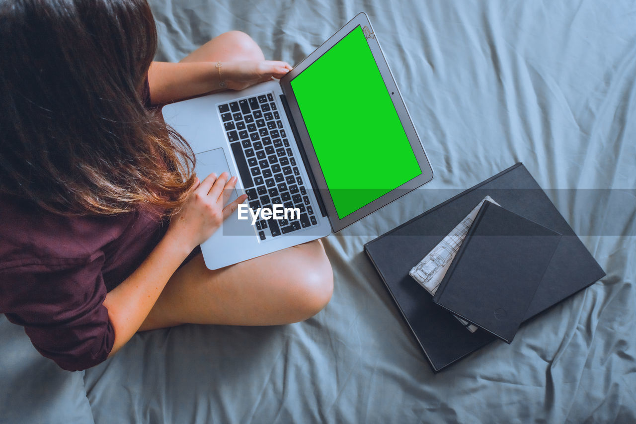 High angle view of woman using laptop while sitting on bed at home