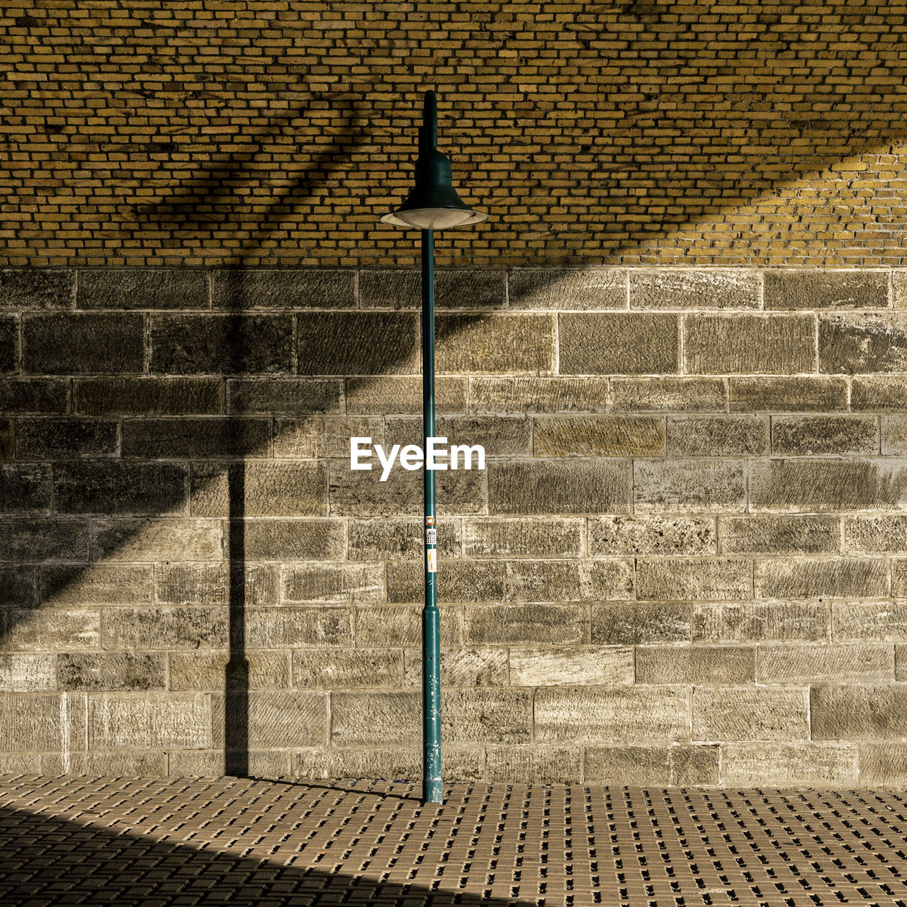 Green street light on sidewalk against brick wall