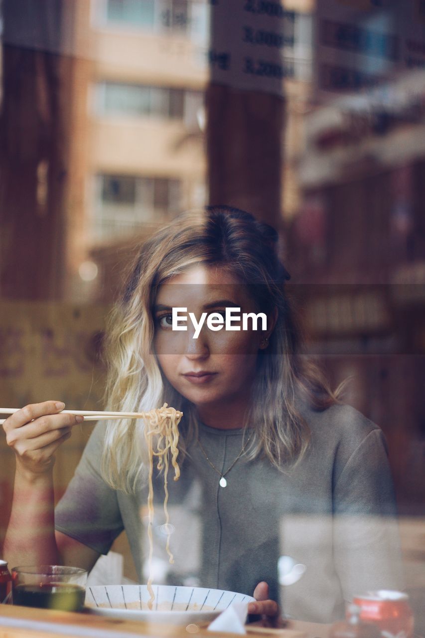 Portrait of young woman holding food in restaurant seen through glass window