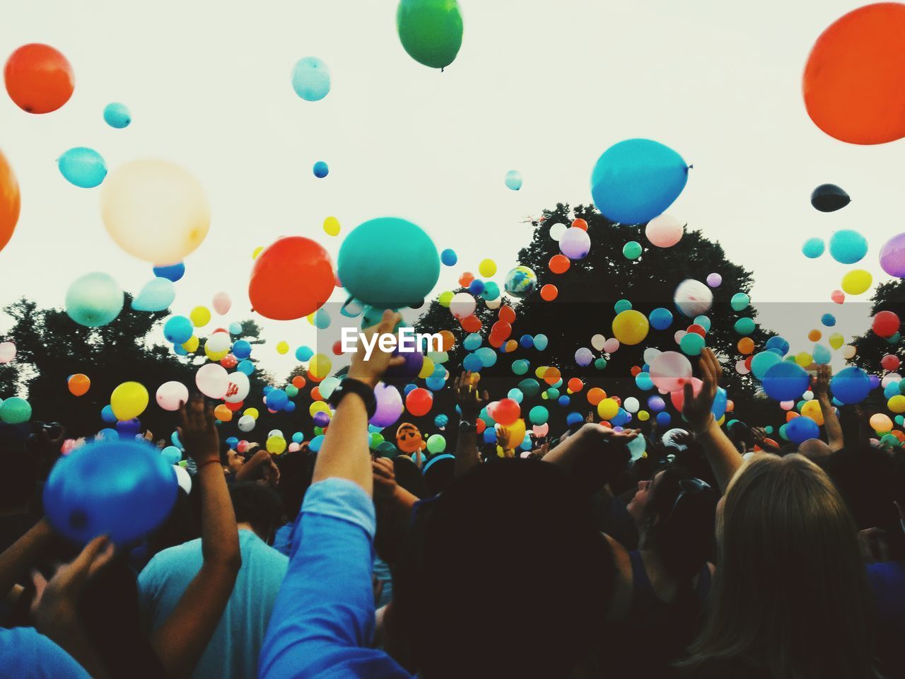 Crowd throwing colorful balloons against sky during festival