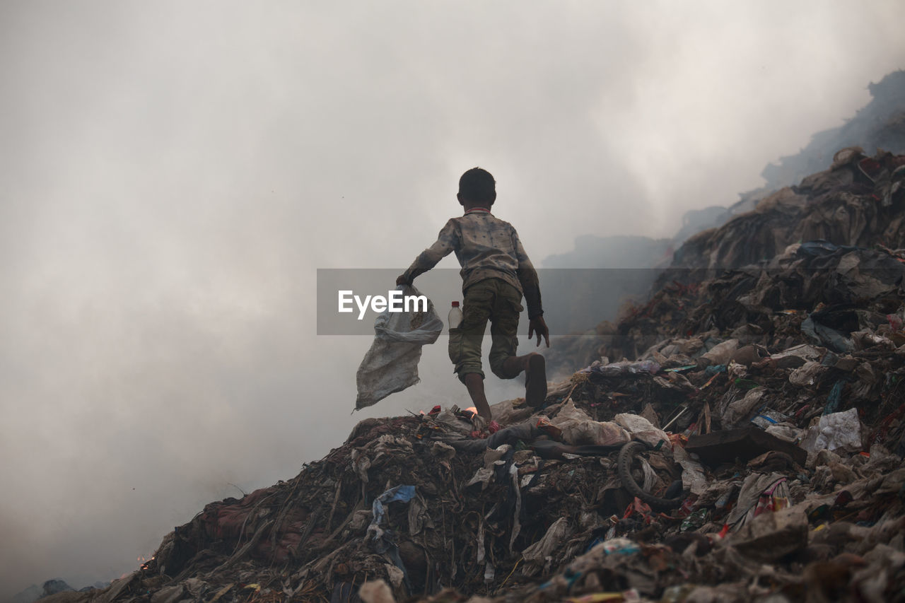 Full length of boy running on garbage dump against sky